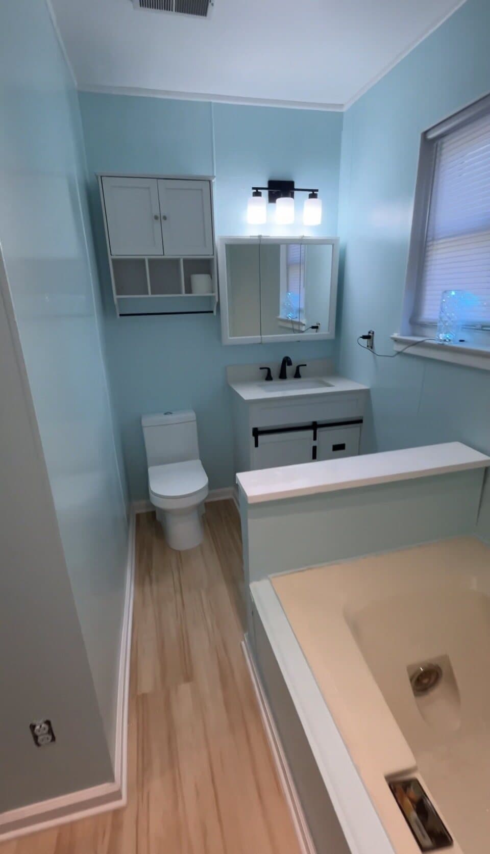 Finished bathroom renovation with blue walls, vanity, tub, and toilet